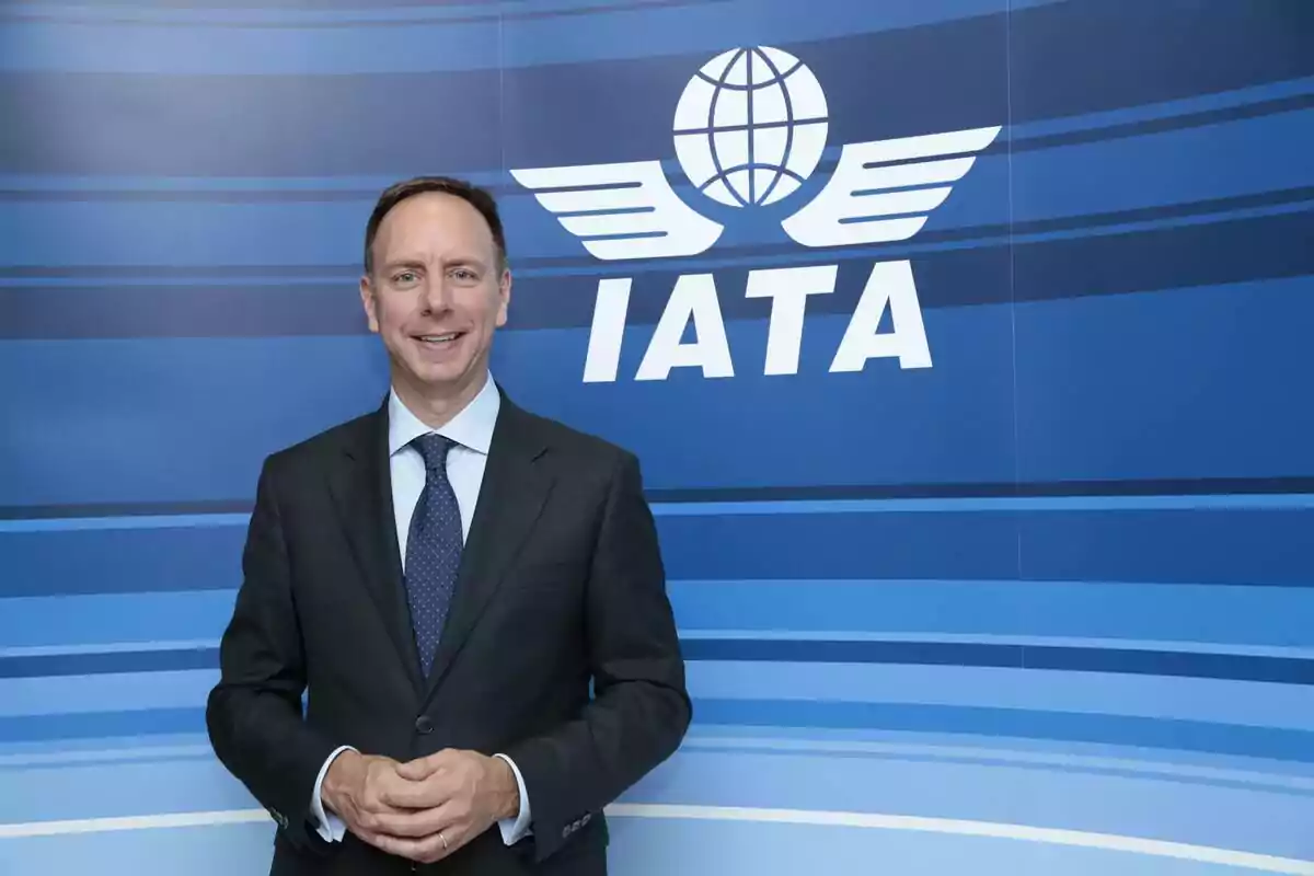 Man in a suit posing in front of a blue background with the IATA logo Man in a suit posing in front of a blue background with the IATA logo