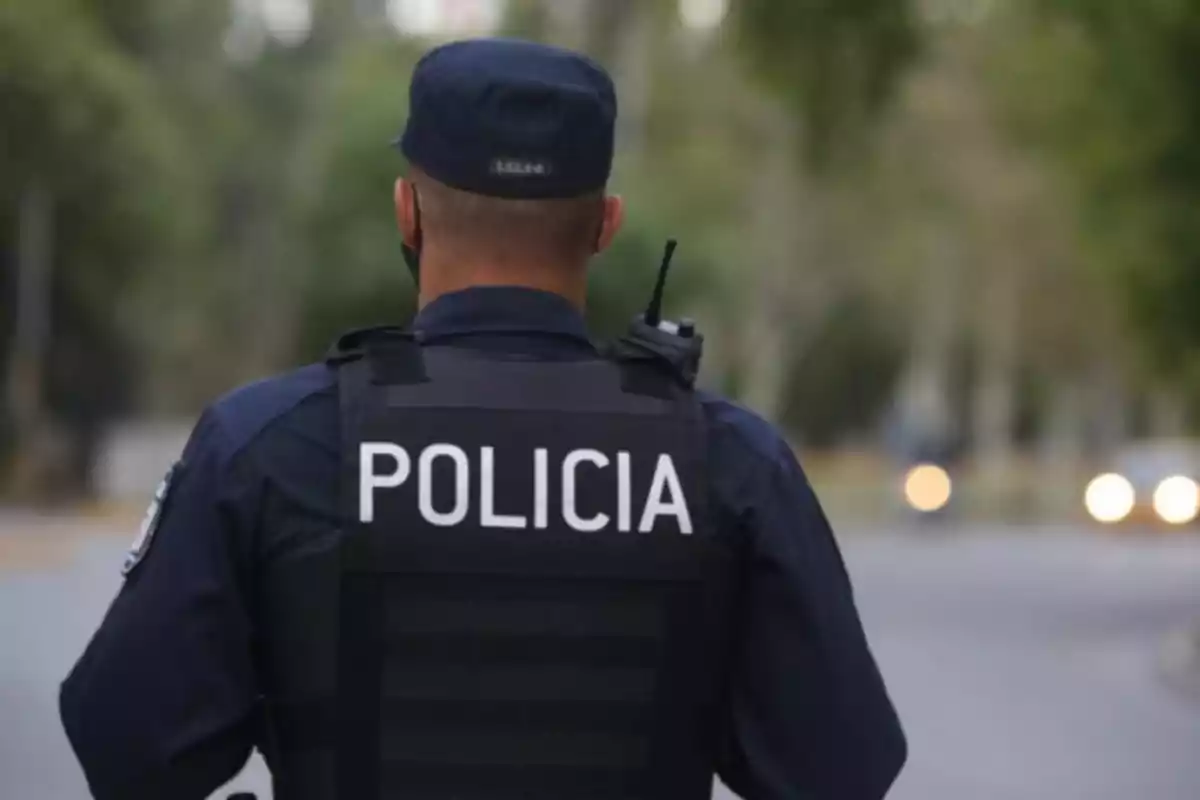 A police officer with his back turned, wearing a bulletproof vest and a radio, walks down a blurred street. A police officer with his back turned, wearing a bulletproof vest and a radio, walks down a blurred street.