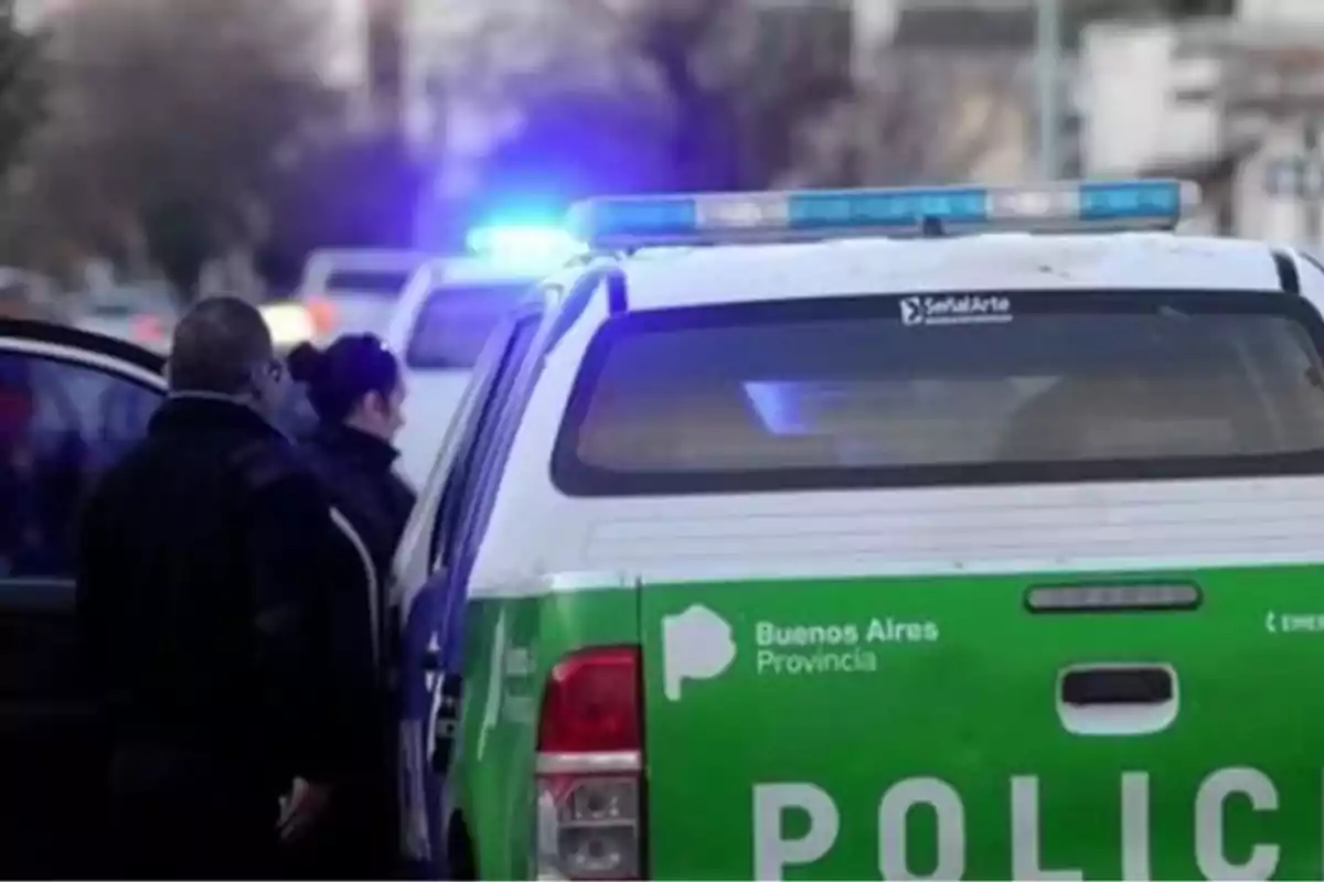 Buenos Aires provincial police patrol car with its lights on and two people next to the vehicle on an urban street Buenos Aires provincial police patrol car with its lights on and two people next to the vehicle on an urban street