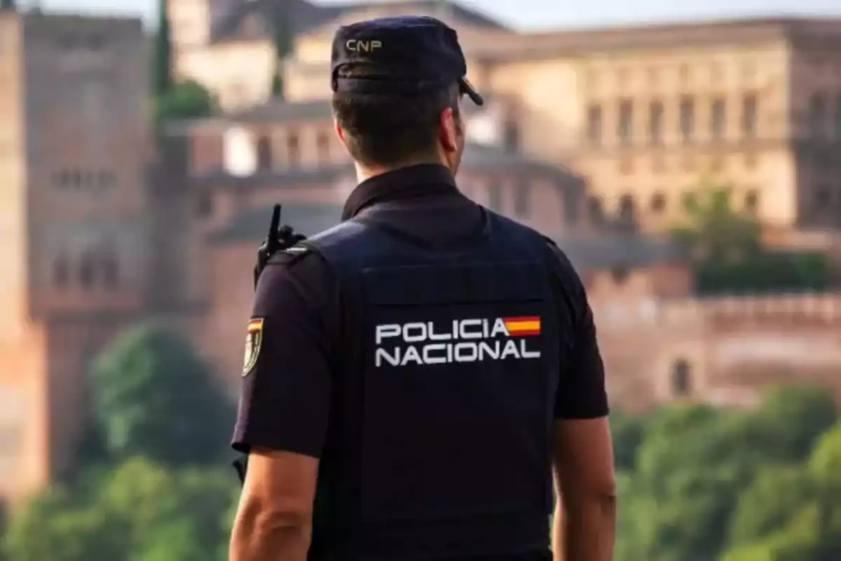 Spanish National Police officer seen from behind, wearing a uniform and vest in an urban area with historic buildings in the background. Spanish National Police officer seen from behind, wearing a uniform and vest in an urban area with historic buildings in the background.