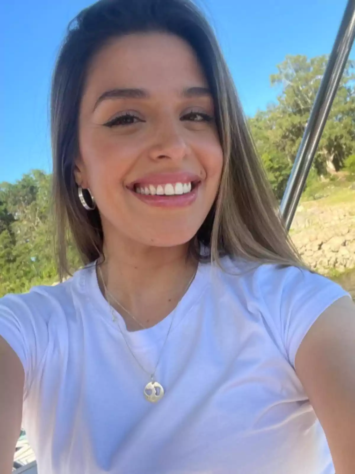 Smiling young man wearing a white t-jersey and a gold necklace taking a selfie outdoors on a sunny day Smiling young man wearing a white t-jersey and a gold necklace taking a selfie outdoors on a sunny day