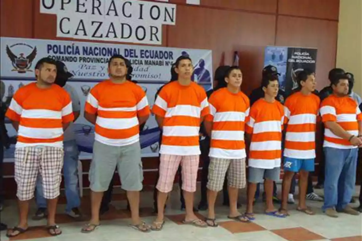 Several men wearing orange and white jerseys are lined up in front of a National Police of Ecuador banner during an official presentation.