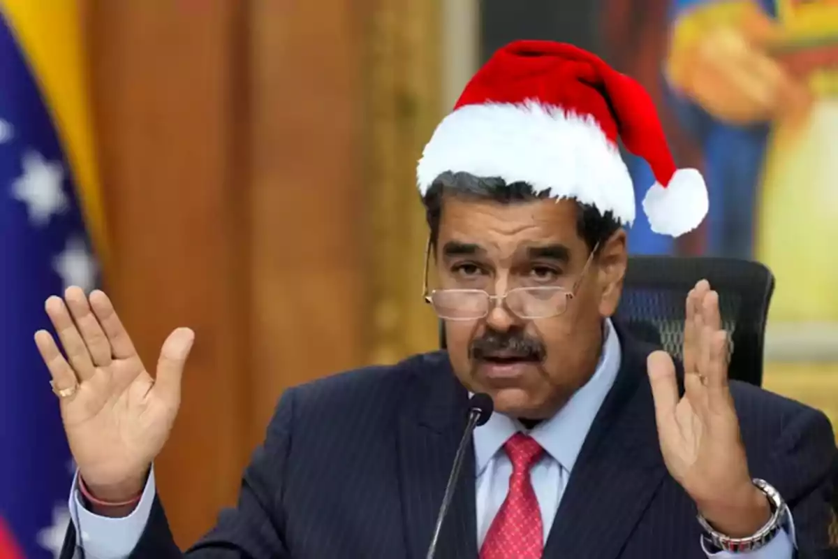 Hombre con gafas y gorro de Navidad hablando frente a un micrófono con las manos levantadas