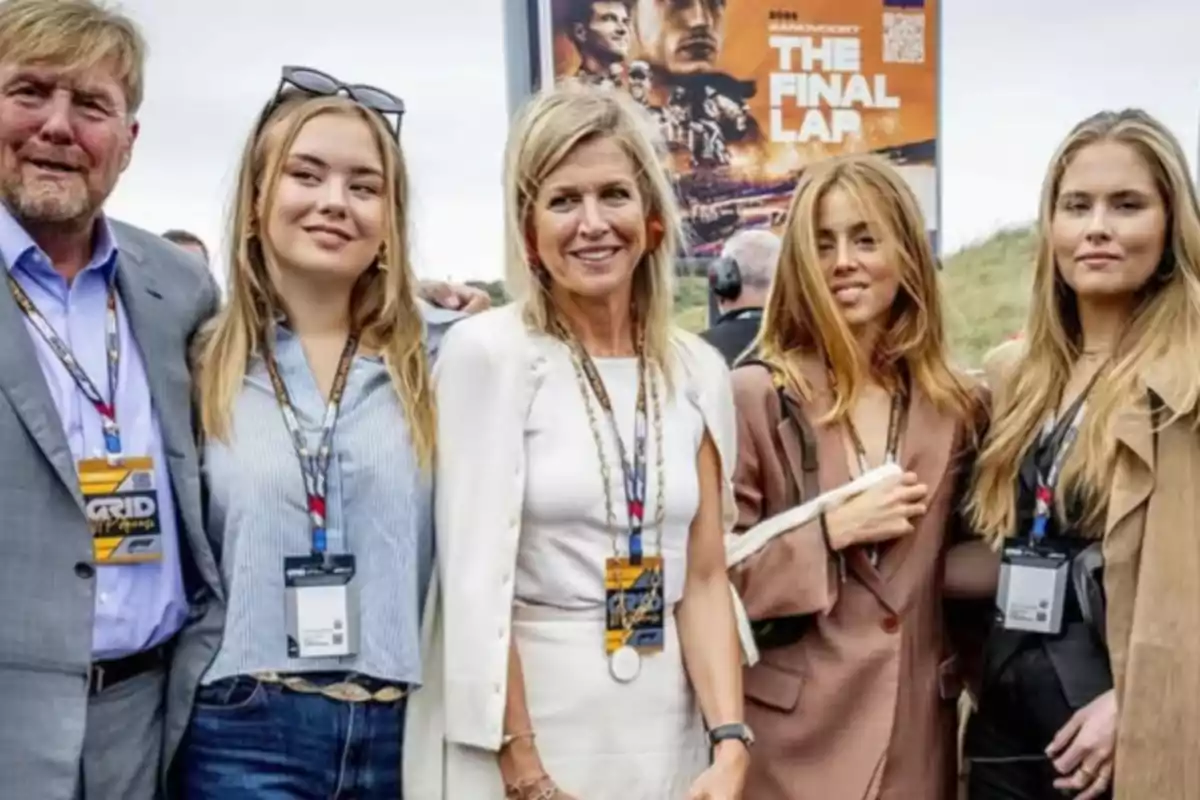 Five people pose smiling in front of an outdoor sports event sign, all wearing badges around their necks and dressed in smart casual attire. Five people pose smiling in front of an outdoor sports event sign, all wearing badges around their necks and dressed in smart casual attire.