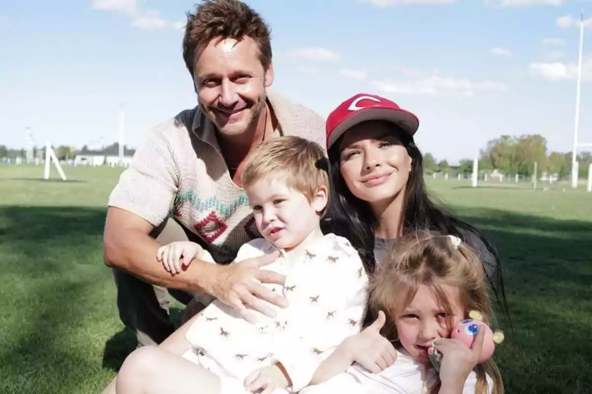 Family of four sitting on the grass in a park enjoying a sunny day