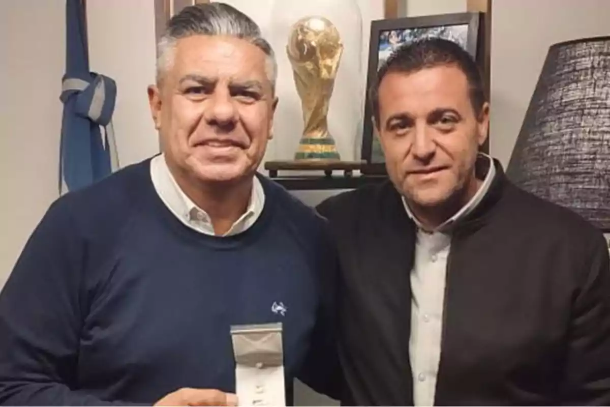 Dos hombres posan juntos en una oficina con una réplica del trofeo de la Copa del Mundo al fondo Dos hombres posan juntos en una oficina con una réplica del trofeo de la Copa del Mundo al fondo