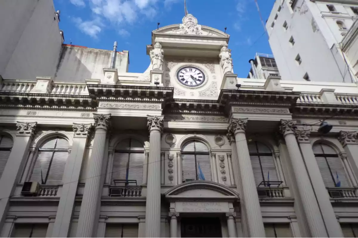 Fachada de un edificio histórico con columnas y un reloj en la parte superior bajo un cielo azul