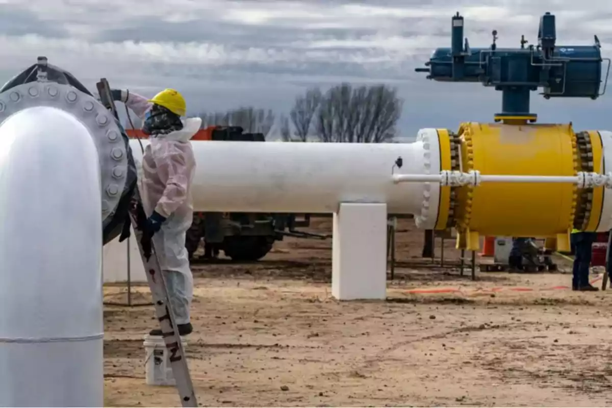 Worker wearing a hard hat and protective gear painting a large industrial pipe in an outdoor setting Worker wearing a hard hat and protective gear painting a large industrial pipe in an outdoor setting