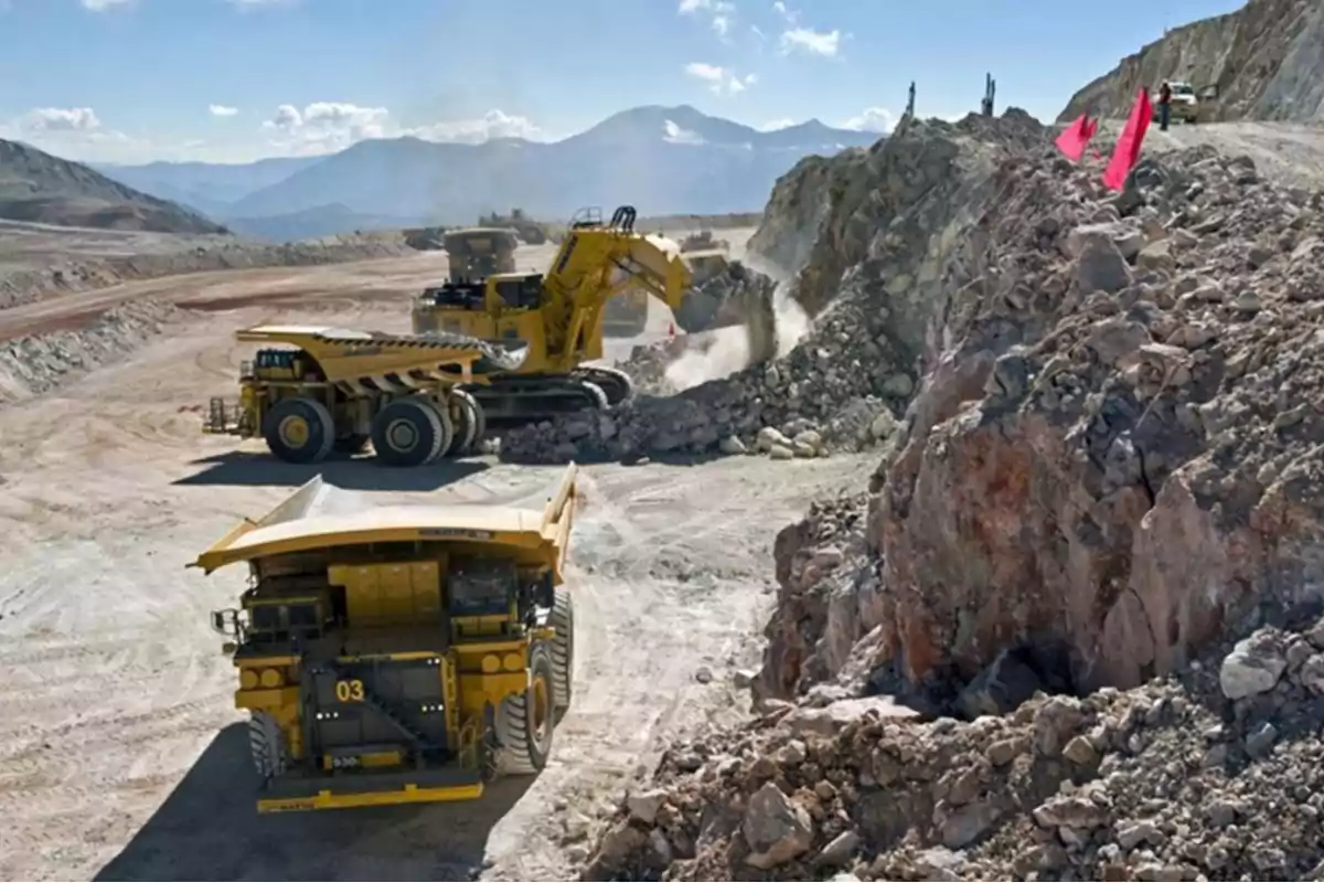 Heavy machinery working in an open-pit mine with mountains in the background and a clear sky. Heavy machinery working in an open-pit mine with mountains in the background and a clear sky.