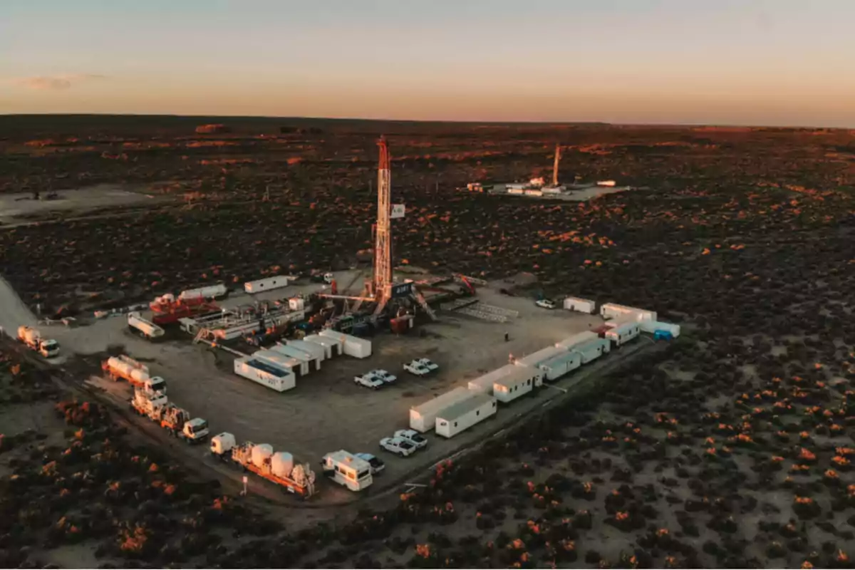 Vista aérea de un yacimiento petrolero en medio del desierto con varias instalaciones, camiones y torres de perforación rodeadas de vegetación baja al atardecer Vista aérea de un yacimiento petrolero en medio del desierto con varias instalaciones, camiones y torres de perforación rodeadas de vegetación baja al atardecer