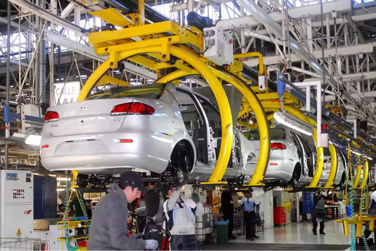 Línea de ensamblaje de automóviles con varios trabajadores y autos en proceso de fabricación dentro de una fábrica industrial Línea de ensamblaje de automóviles con varios trabajadores y autos en proceso de fabricación dentro de una fábrica industrial