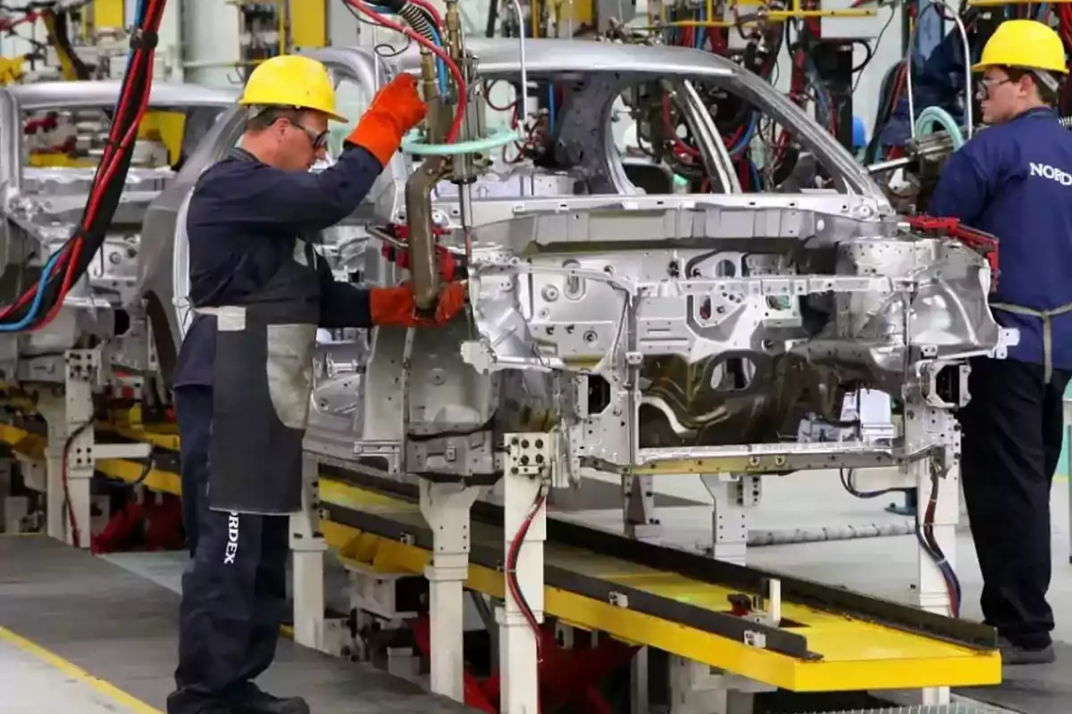 Trabajadores ensamblando la carrocería de un automóvil en una línea de producción industrial usando equipo de protección