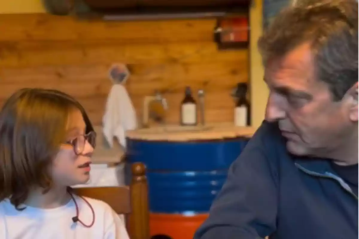 A man and a girl with glasses are talking while sitting in a room with wooden walls and objects in the background. A man and a girl with glasses are talking while sitting in a room with wooden walls and objects in the background.