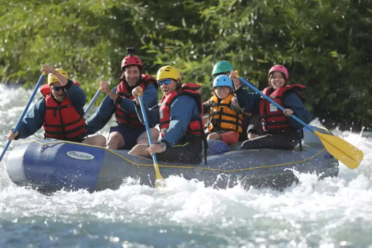 Grupo de personas con chalecos salvavidas y cascos remando en una balsa inflable sobre aguas rápidas rodeados de vegetación Grupo de personas con chalecos salvavidas y cascos remando en una balsa inflable sobre aguas rápidas rodeados de vegetación