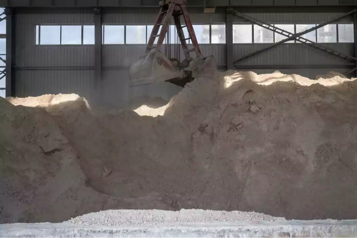 A large industrial shovel collects sand inside a factory lit by windows. A large industrial shovel collects sand inside a factory lit by windows.