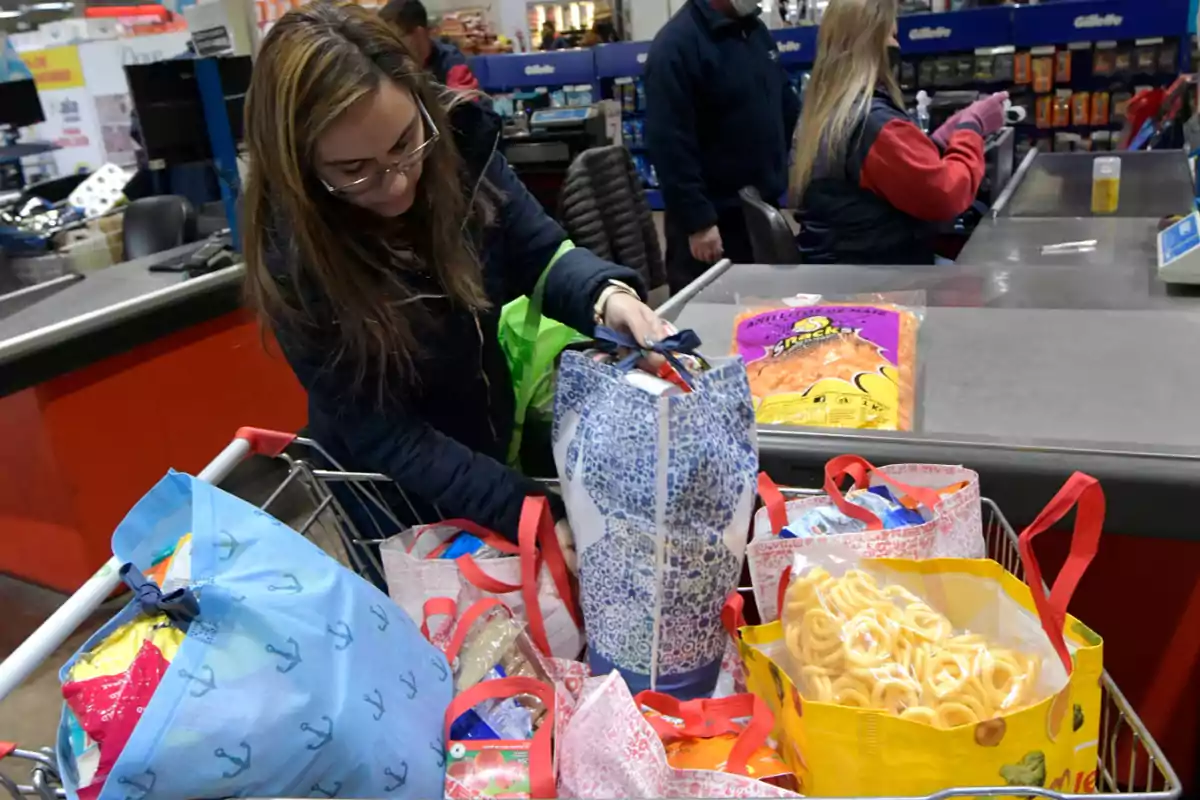Woman packing her groceries into reusable bags at the checkout of a supermarket Woman packing her groceries into reusable bags at the checkout of a supermarket