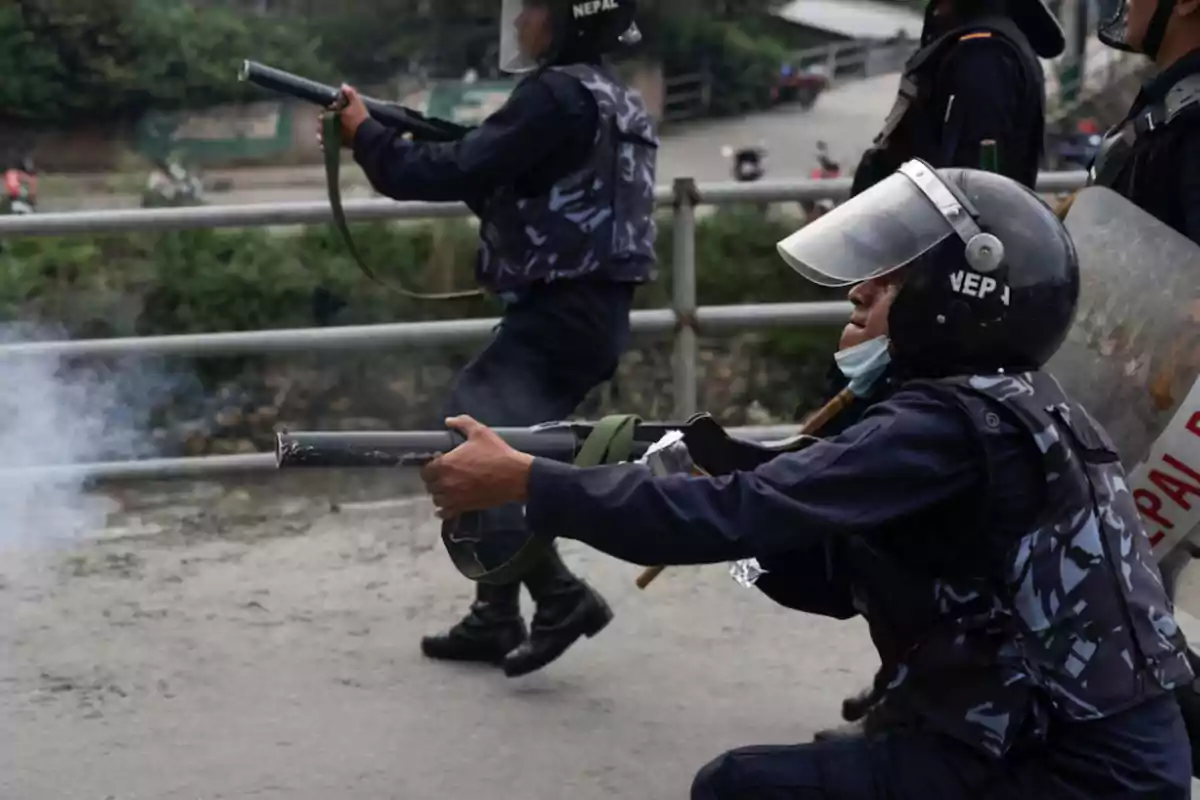 Policías antidisturbios con equipo de protección disparando gases lacrimógenos en una calle