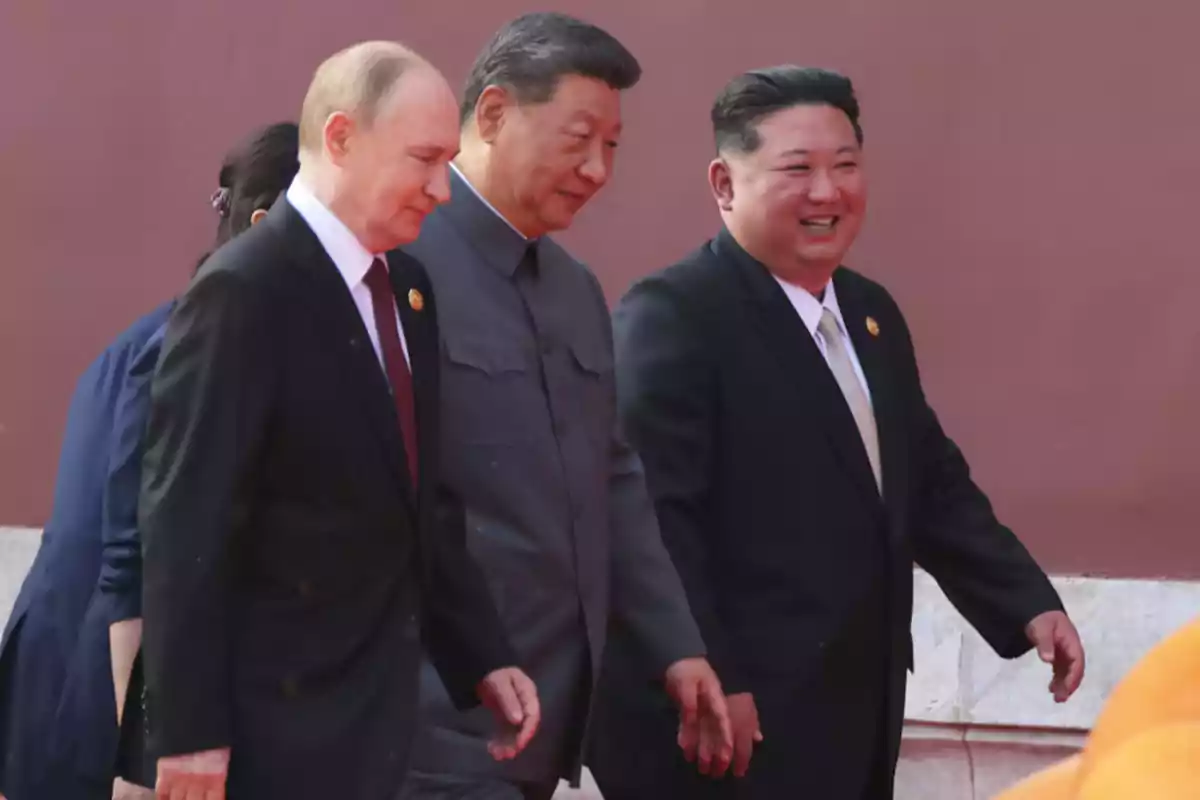 Three men in suits walk together and talk while smiling in front of a red wall. Three men in suits walk together and talk while smiling in front of a red wall.