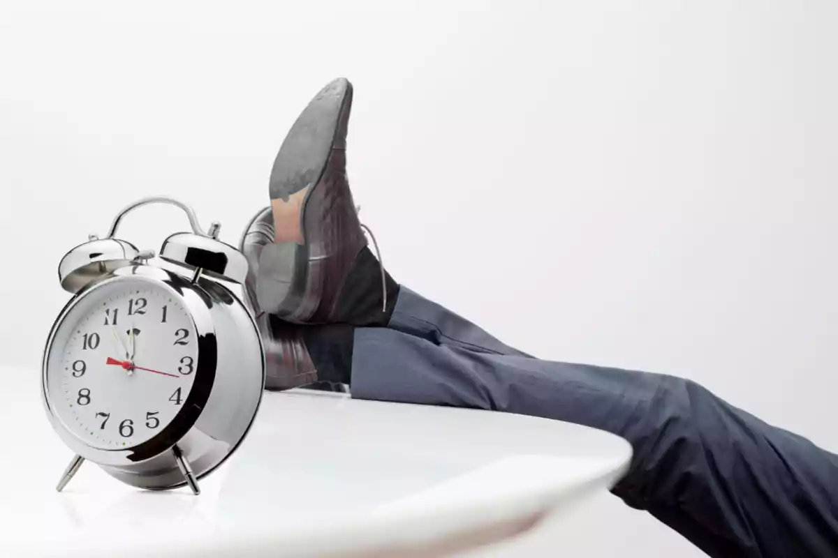 A man in a suit has his feet on a desk next to a large alarm clock. A man in a suit has his feet on a desk next to a large alarm clock.