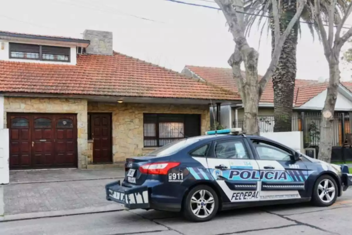 Police patrol car parked in front of a stone-fronted house with a red-tiled roof and trees on the sidewalk Police patrol car parked in front of a stone-fronted house with a red-tiled roof and trees on the sidewalk