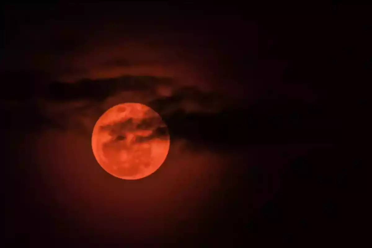 Luna llena de color rojo anaranjado parcialmente cubierta por nubes oscuras en el cielo nocturno Luna llena de color rojo anaranjado parcialmente cubierta por nubes oscuras en el cielo nocturno