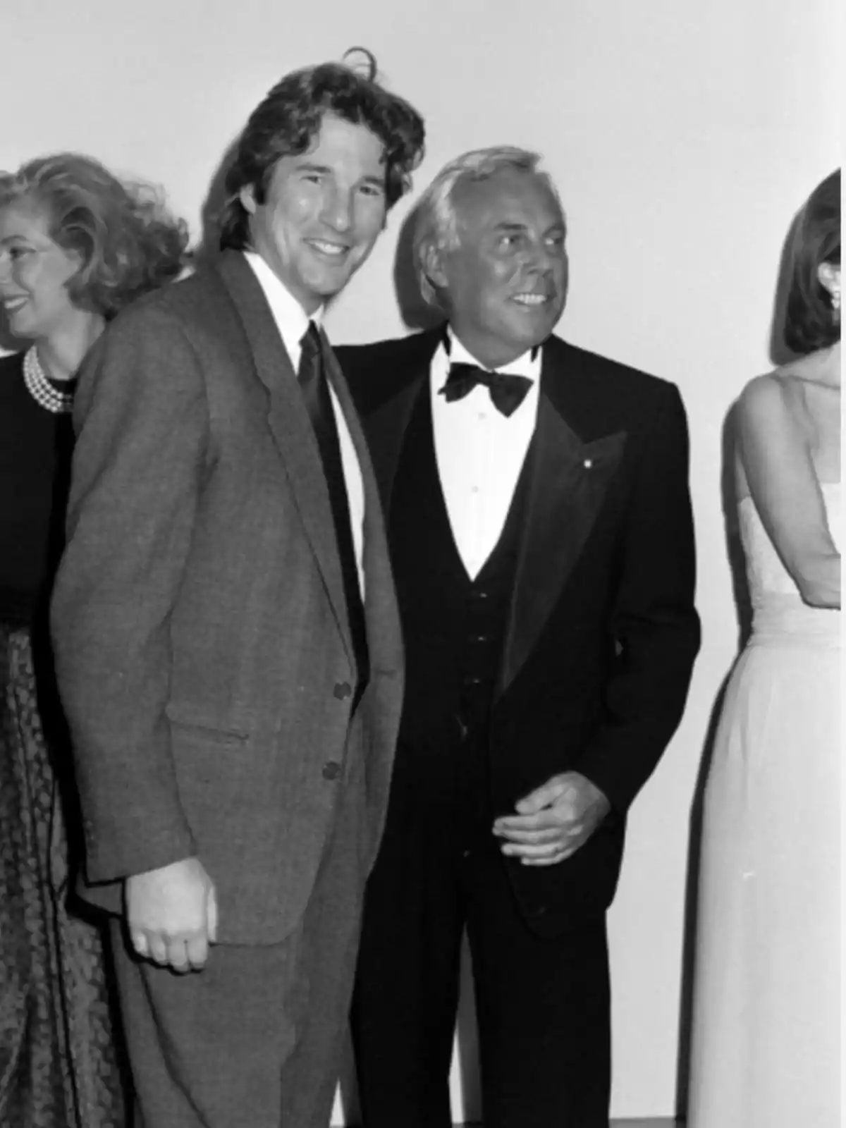Dos hombres elegantemente vestidos posan sonrientes en un evento social junto a otras personas Dos hombres elegantemente vestidos posan sonrientes en un evento social junto a otras personas