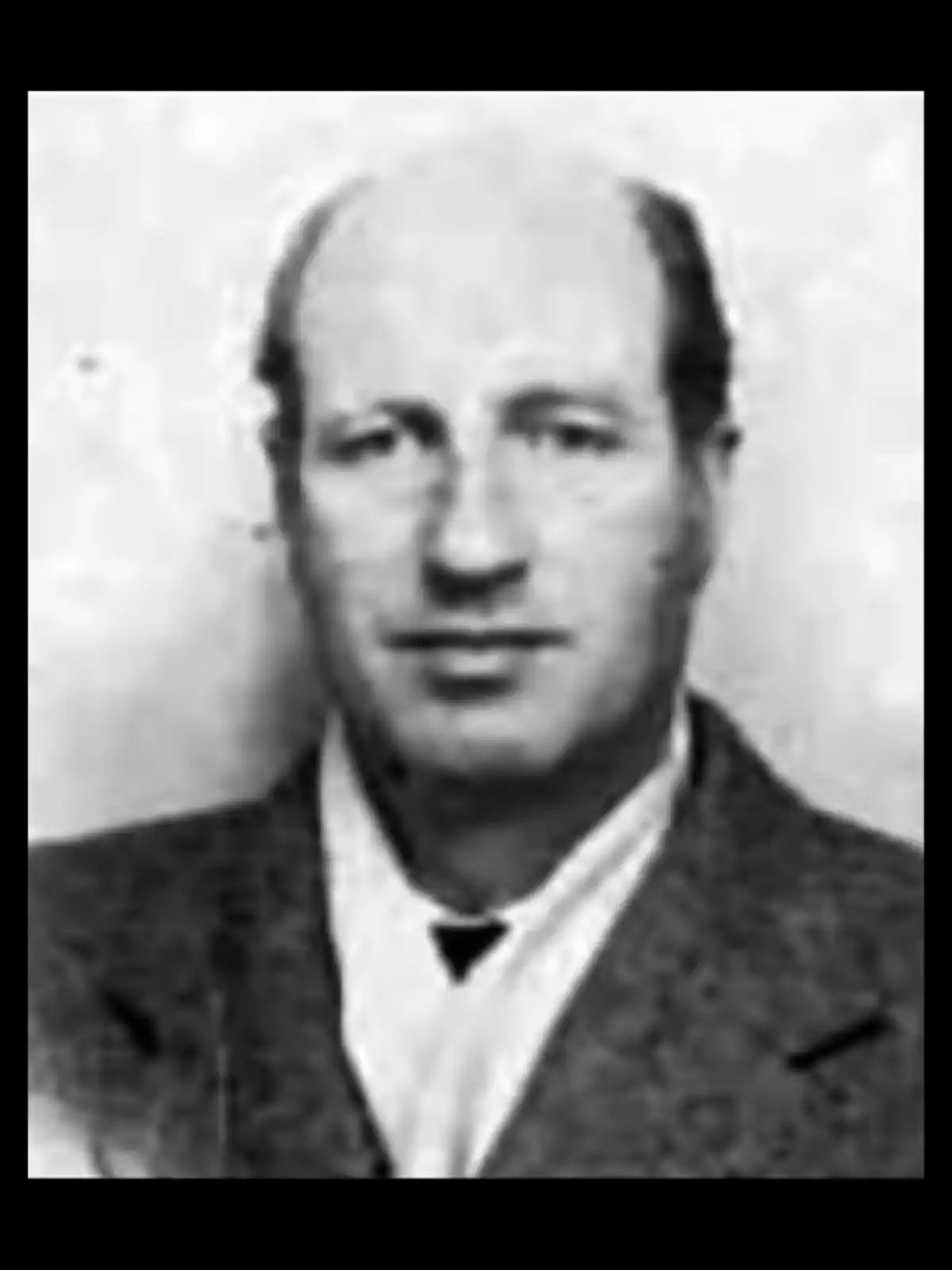 Black and white photograph of a middle-aged man with short hair and a broad forehead, wearing a jacket and a light-colored jersey Black and white photograph of a middle-aged man with short hair and a broad forehead, wearing a jacket and a light-colored jersey