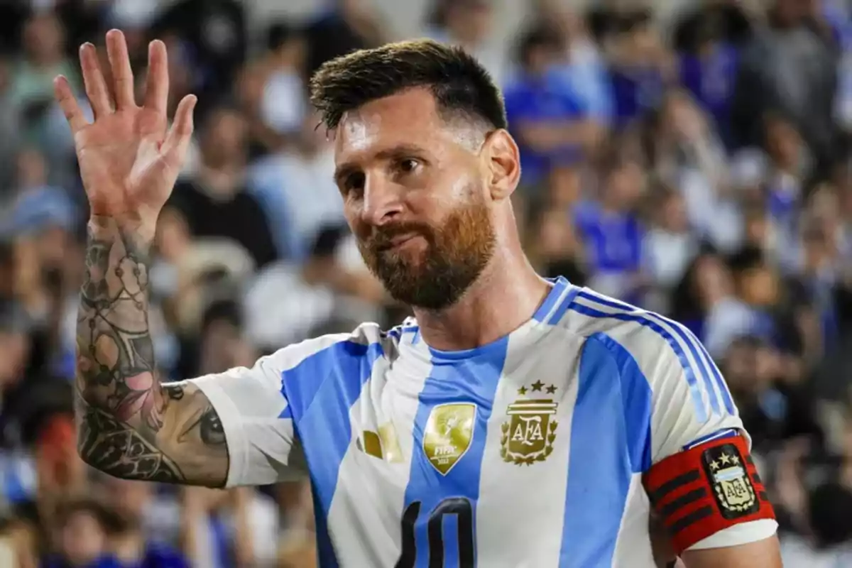 Argentine player with a beard and tattoos on his right arm greets the crowd wearing the Argentina national team jersey and a red captain's armband. Argentine player with a beard and tattoos on his right arm greets the crowd wearing the Argentina national team jersey and a red captain's armband.