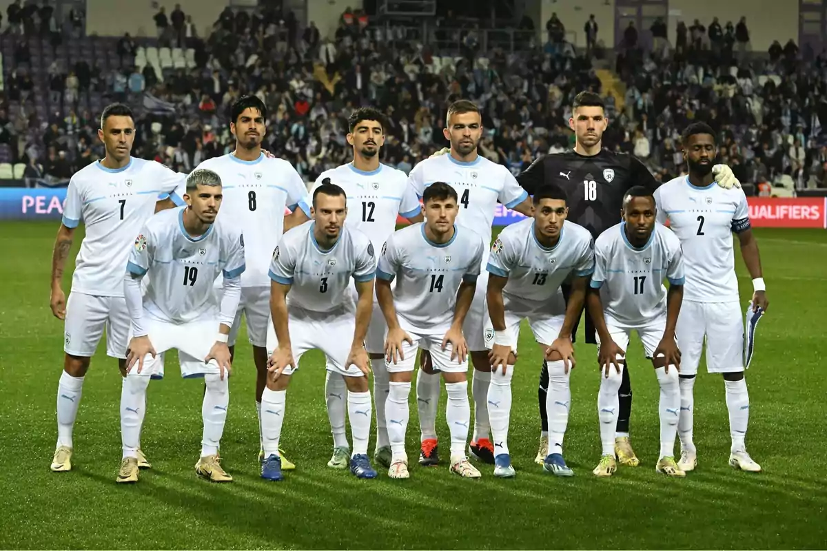 Once jugadores de fútbol posan juntos en el campo antes de un partido con uniformes blancos y celestes mientras el público observa desde las gradas