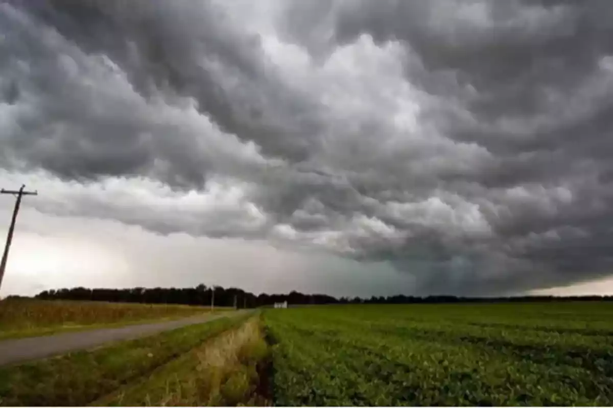 Cielo cubierto de nubes oscuras sobre un campo verde y una carretera rural Cielo cubierto de nubes oscuras sobre un campo verde y una carretera rural