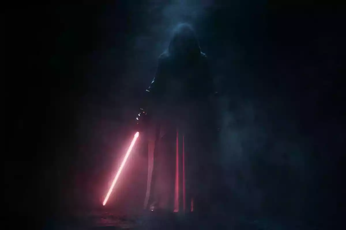 Figura encapuchada sosteniendo un sable de luz rojo en medio de la oscuridad y el humo Figura encapuchada sosteniendo un sable de luz rojo en medio de la oscuridad y el humo
