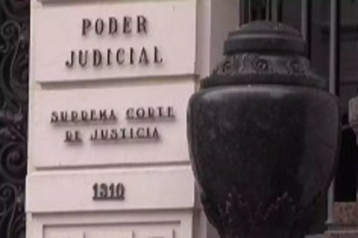 Fachada de un edificio con letrero que dice Poder Judicial Suprema Corte de Justicia y el número 1510 junto a una estructura decorativa oscura Fachada de un edificio con letrero que dice Poder Judicial Suprema Corte de Justicia y el número 1510 junto a una estructura decorativa oscura