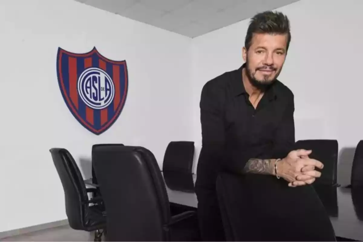 Bearded man with short hair leaning on a chair inside a meeting room with the San Lorenzo crest on the wall.