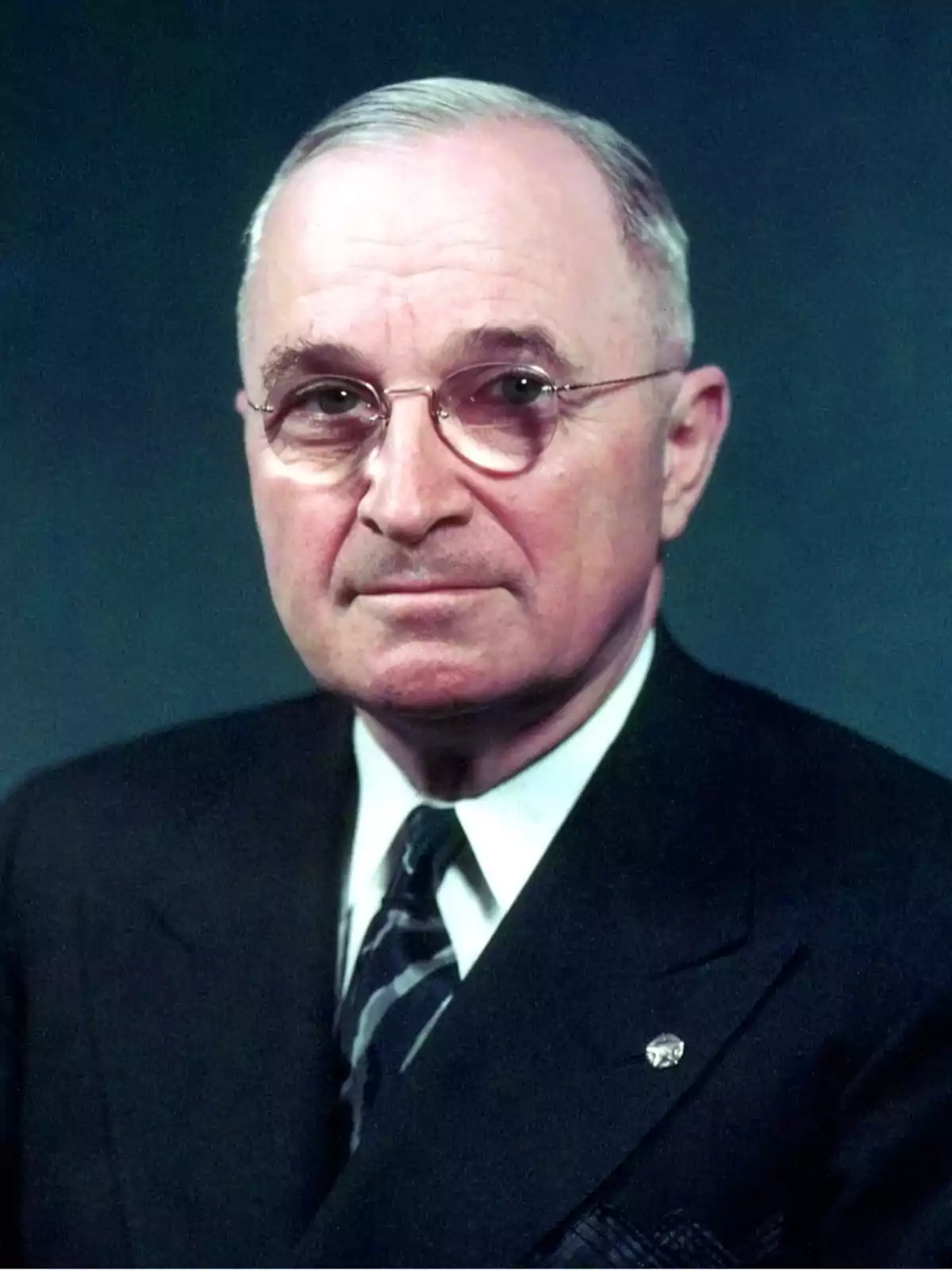 Hombre mayor con gafas y cabello canoso peinado hacia un lado viste traje oscuro y corbata sobre fondo liso azul Hombre mayor con gafas y cabello canoso peinado hacia un lado viste traje oscuro y corbata sobre fondo liso azul