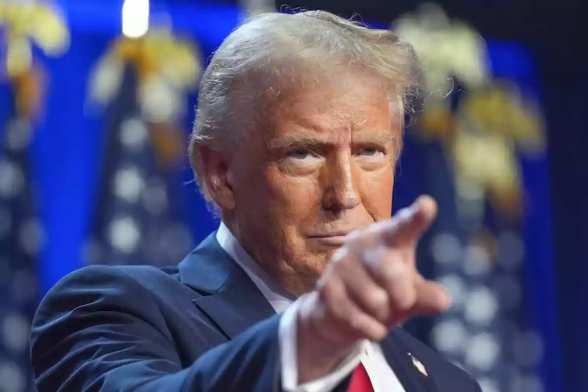 Blond-haired man in a blue suit pointing forward with blurred flags in the background Blond-haired man in a blue suit pointing forward with blurred flags in the background