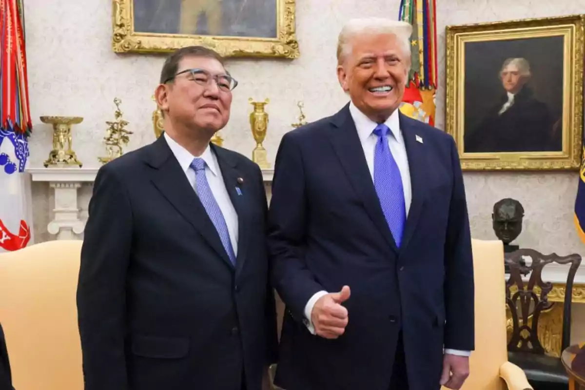 Two men in dark suits pose smiling in an elegant office, one of them giving a thumbs-up gesture, with paintings and flags visible in the background. Two men in dark suits pose smiling in an elegant office, one of them giving a thumbs-up gesture, with paintings and flags visible in the background.