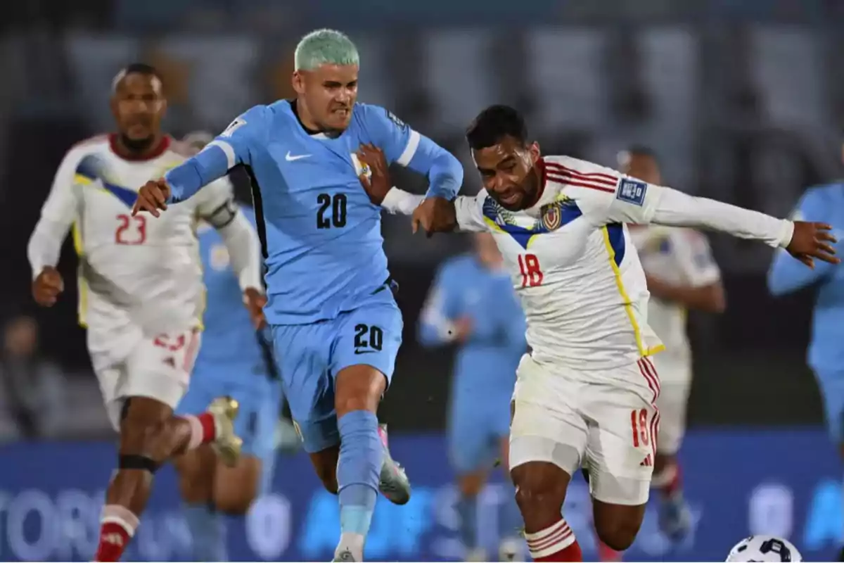 Two players compete for the ball during an international match, one wearing a light blue uniform and the other wearing a white uniform. Two players compete for the ball during an international match, one wearing a light blue uniform and the other wearing a white uniform.