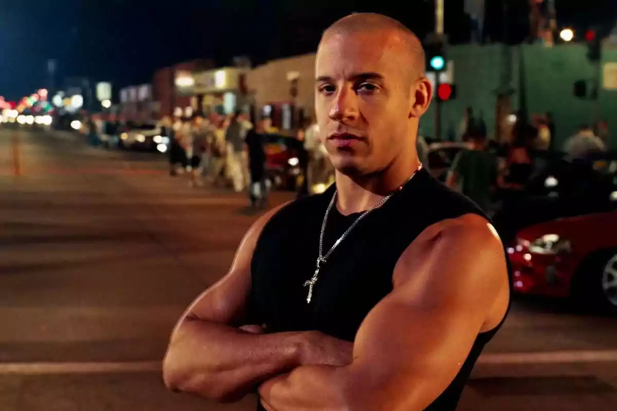 Muscular man wearing a black tank top and a cross necklace standing on a street lit up at night with cars and people in the background Muscular man wearing a black tank top and a cross necklace standing on a street lit up at night with cars and people in the background