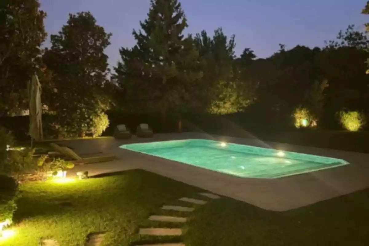 Piscina iluminada en un jardín rodeado de árboles al anochecer Piscina iluminada en un jardín rodeado de árboles al anochecer