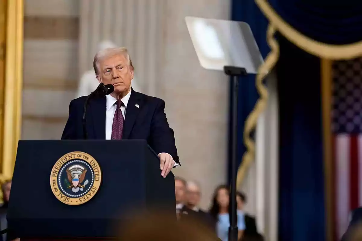 Hombre de cabello rubio con traje oscuro hablando en un podio presidencial en un recinto oficial Hombre de cabello rubio con traje oscuro hablando en un podio presidencial en un recinto oficial