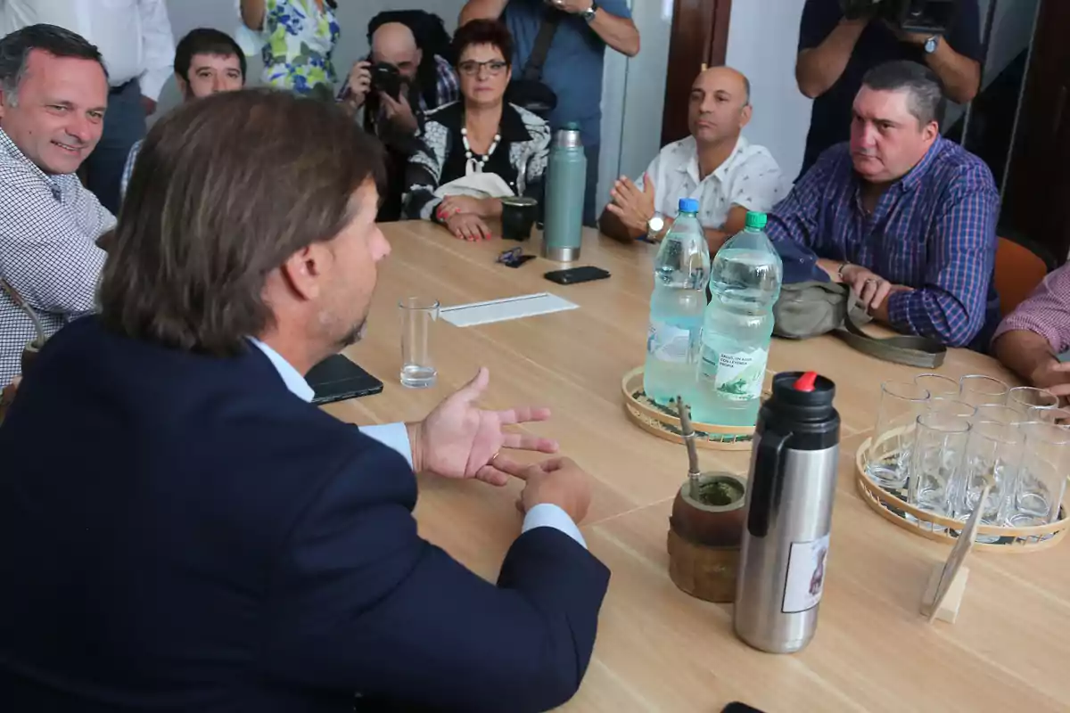 Un grupo de personas sentadas alrededor de una mesa en una reunión, con botellas de agua y un termo de mate en el centro.