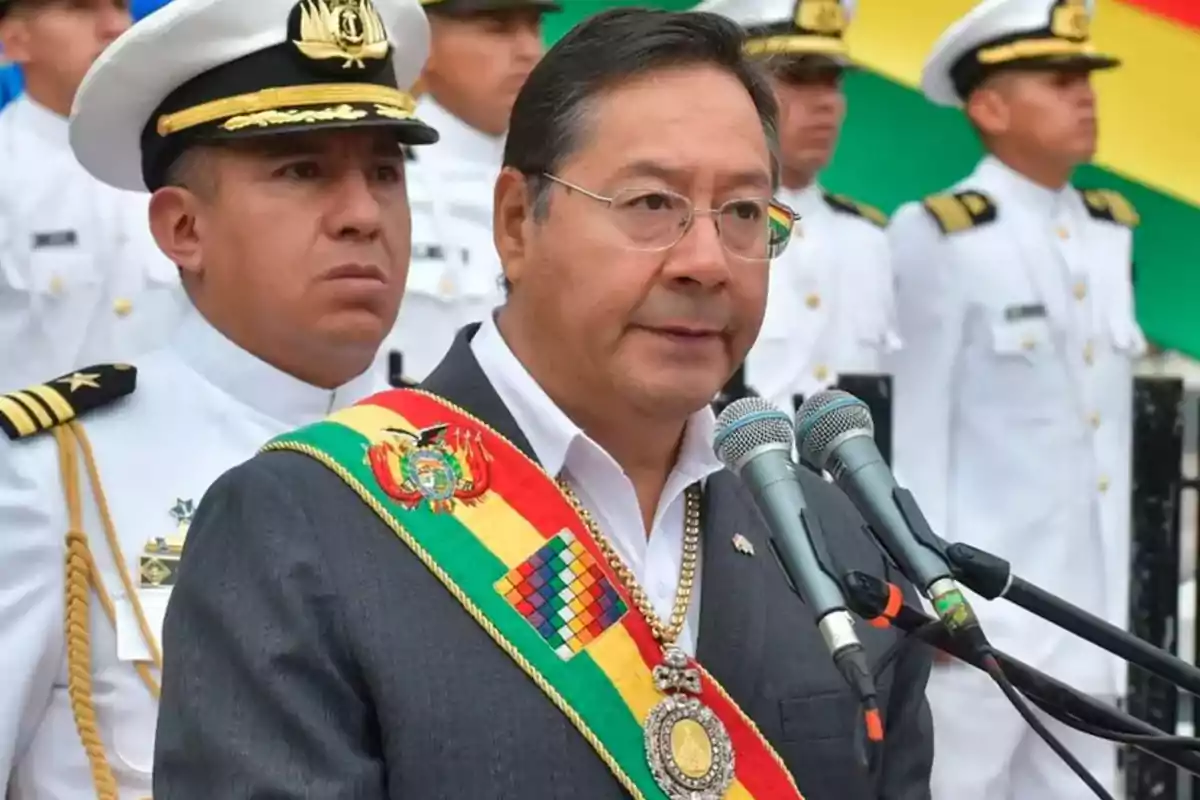A man with a presidential sash speaks in front of microphones accompanied by naval officers. A man with a presidential sash speaks in front of microphones accompanied by naval officers.