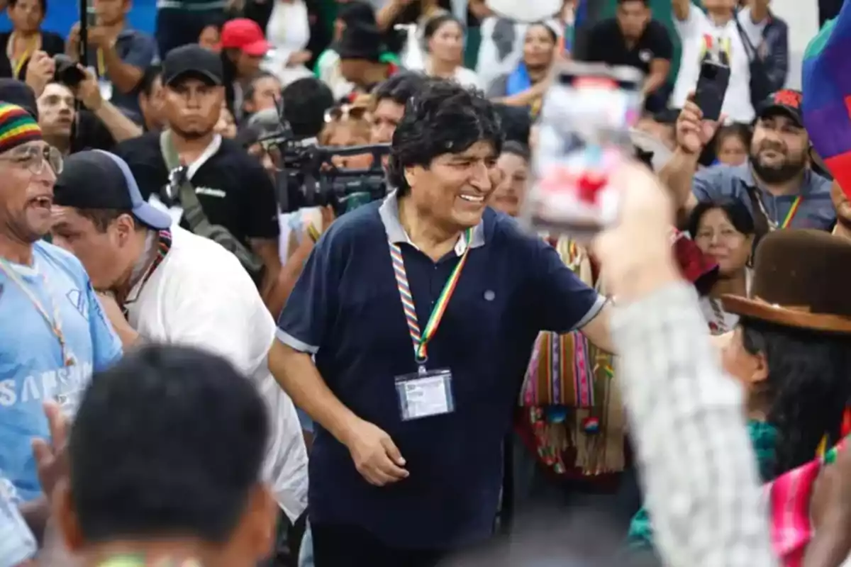 Un hombre sonríe mientras saluda a una multitud en un evento público, rodeado de personas que lo observan y algunos que toman fotos. Un hombre sonríe mientras saluda a una multitud en un evento público, rodeado de personas que lo observan y algunos que toman fotos.