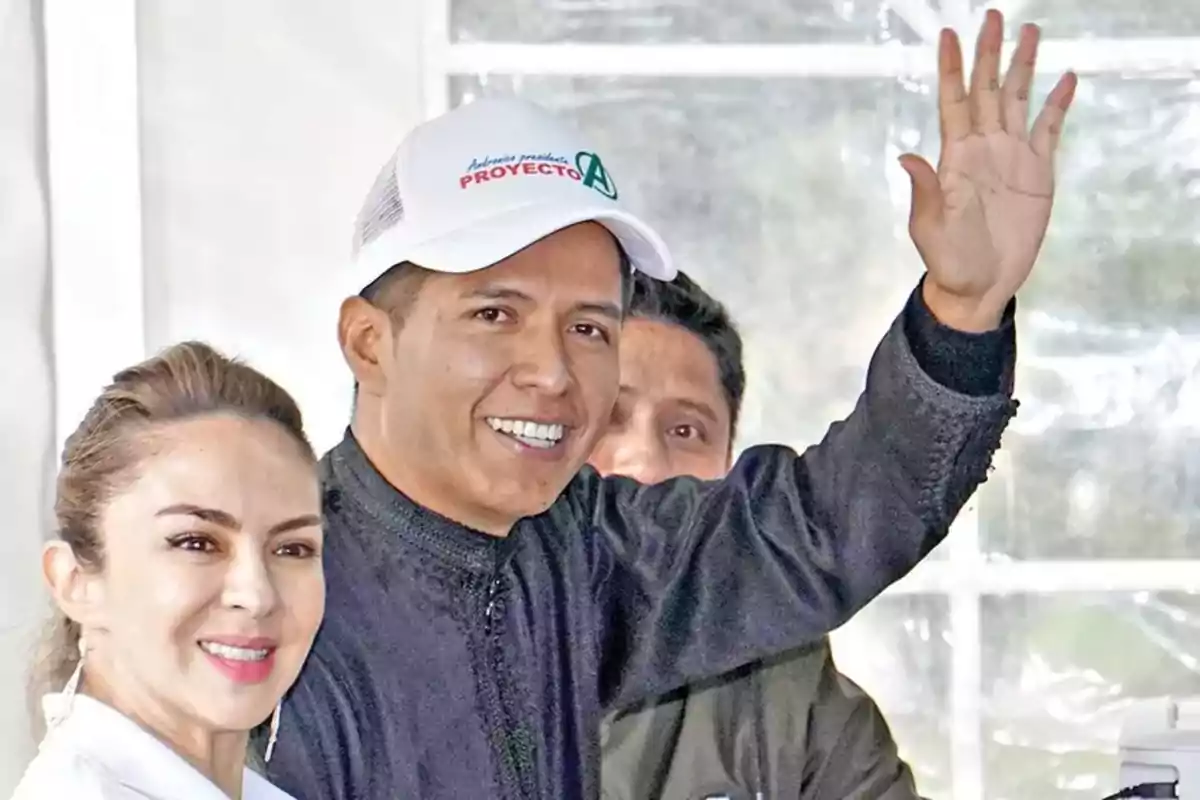 A man wearing a white cap smiles and waves while a woman next to him also smiles. A man wearing a white cap smiles and waves while a woman next to him also smiles.