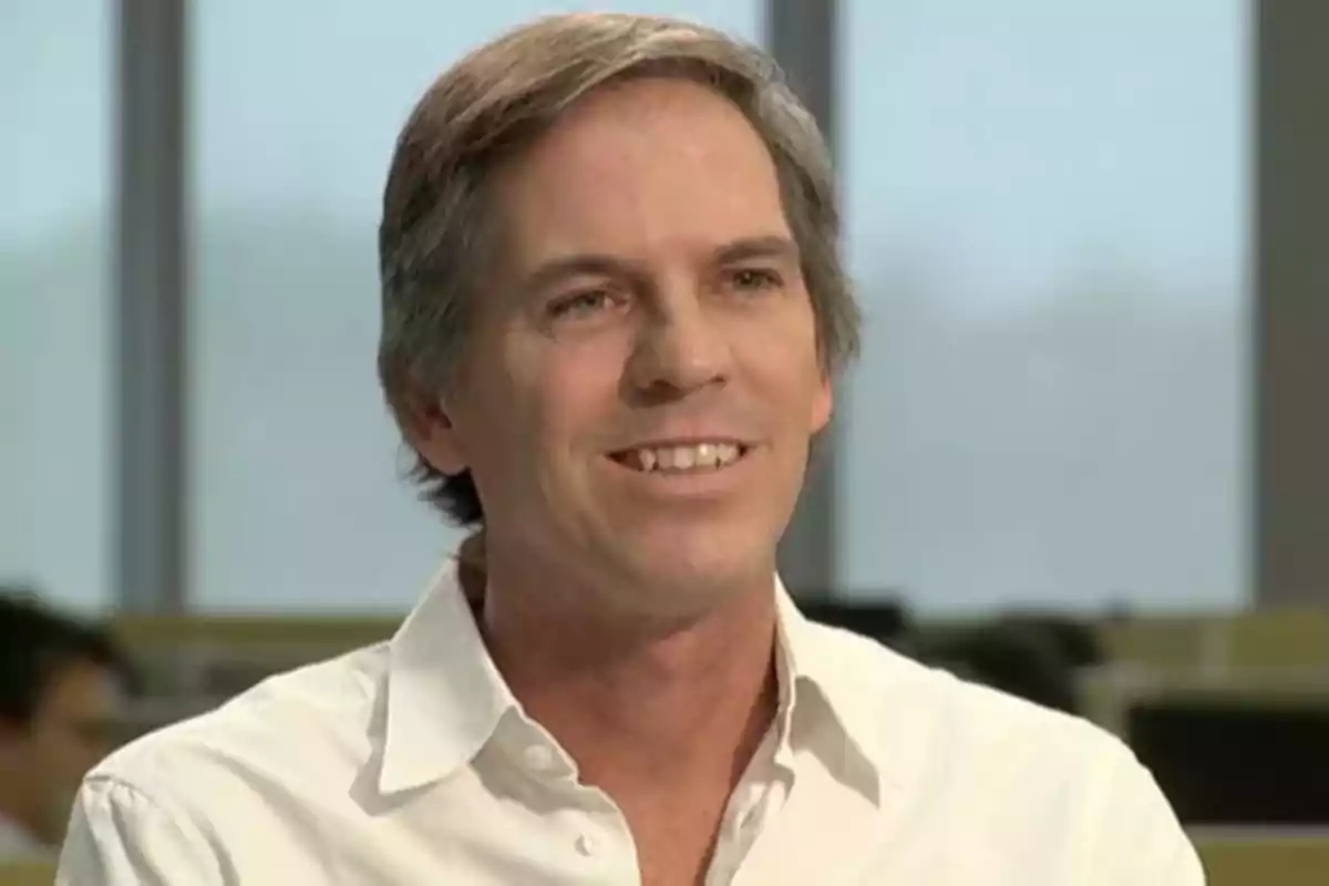 Hombre sonriendo con camisa blanca en un entorno de oficina.