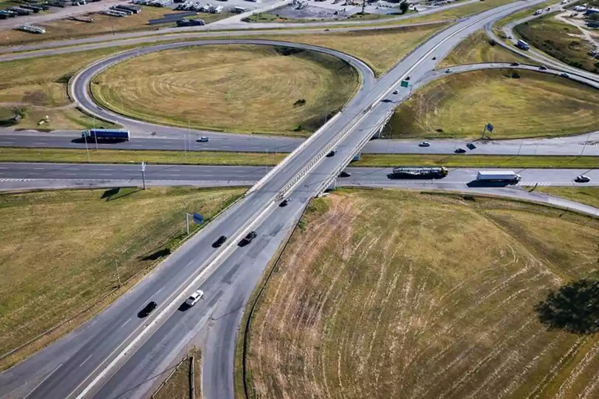Vista aérea de un cruce de autopistas con varios carriles y vehículos circulando rodeado de áreas verdes