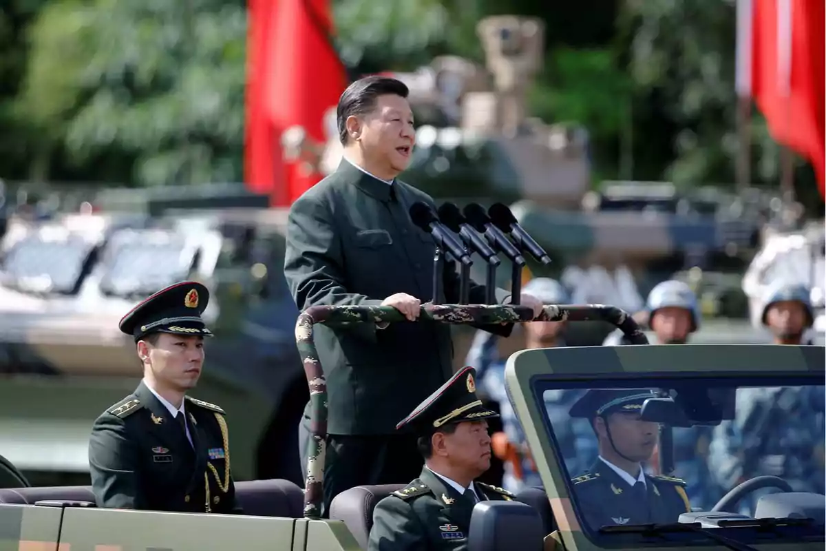 A man in military uniform gives a speech from a vehicle accompanied by officers while soldiers and red flags can be seen in the background. A man in military uniform gives a speech from a vehicle accompanied by officers while soldiers and red flags can be seen in the background.