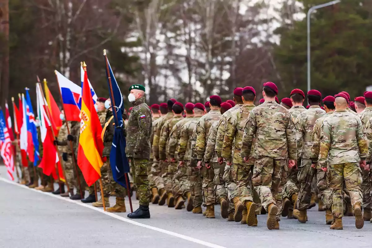 Soldiers marching in formation alongside a row of people holding flags from different countries in an outdoor setting. Soldiers marching in formation alongside a row of people holding flags from different countries in an outdoor setting.