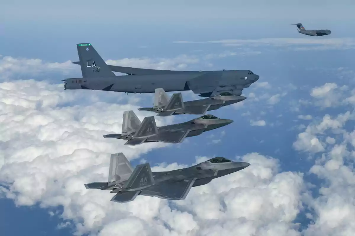Cuatro aviones de combate y un avión de transporte militar vuelan en formación sobre un mar de nubes en el cielo azul