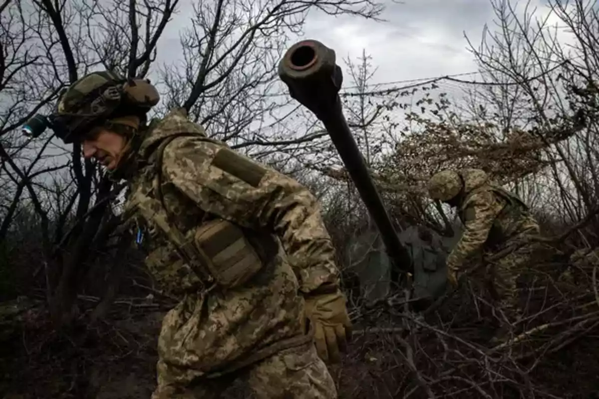 Soldados en uniforme de camuflaje caminan entre árboles secos en un entorno boscoso.